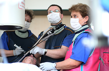 Mann unf Frau mit Mundschutz untersuchen liegenden Patienten in der Pneumologie durch den Mund, Endoskopie